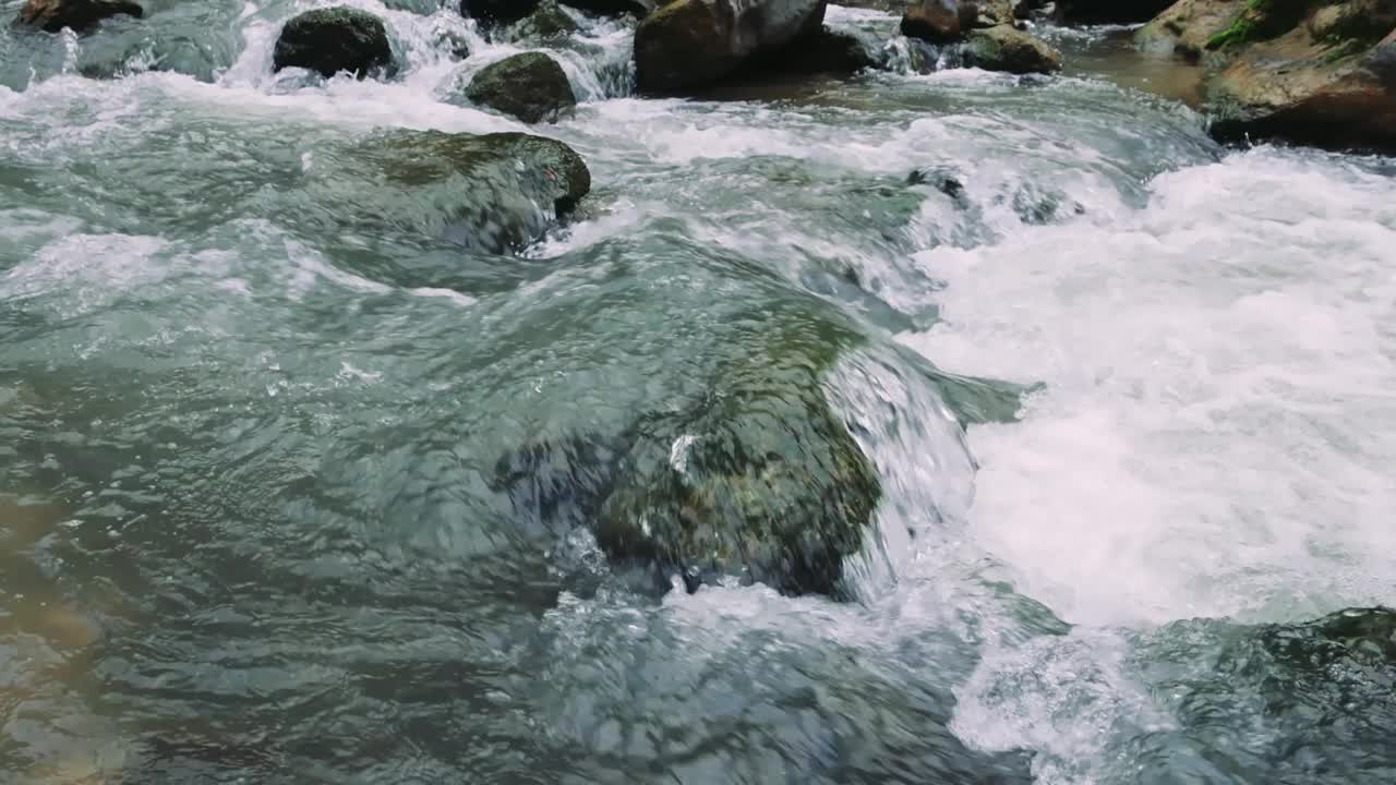 山间小溪湍急地流过石头，自然湍急。小溪在清澈的山间流过石头。山间石砌小溪，清澈见底，水流湍急视频素材