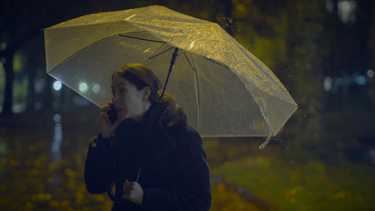 愤怒的年轻女子在下雨的城市晚上用智能手机争吵视频素材