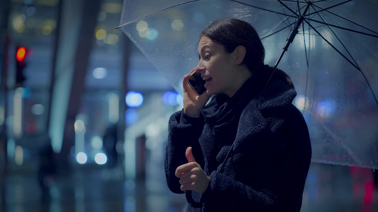 愤怒的年轻女子在下雨的城市晚上用智能手机争吵视频素材