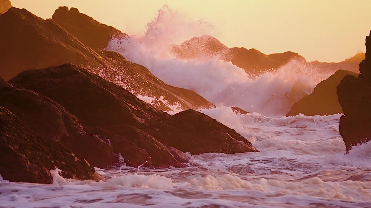 粗糙的海浪吹在岩石的背景。日落时的海滩。慢动作视频素材