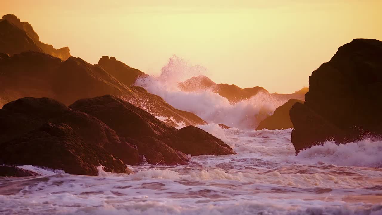 日落时分，海浪冲击着海滩上的岩石。-广角镜头视频素材