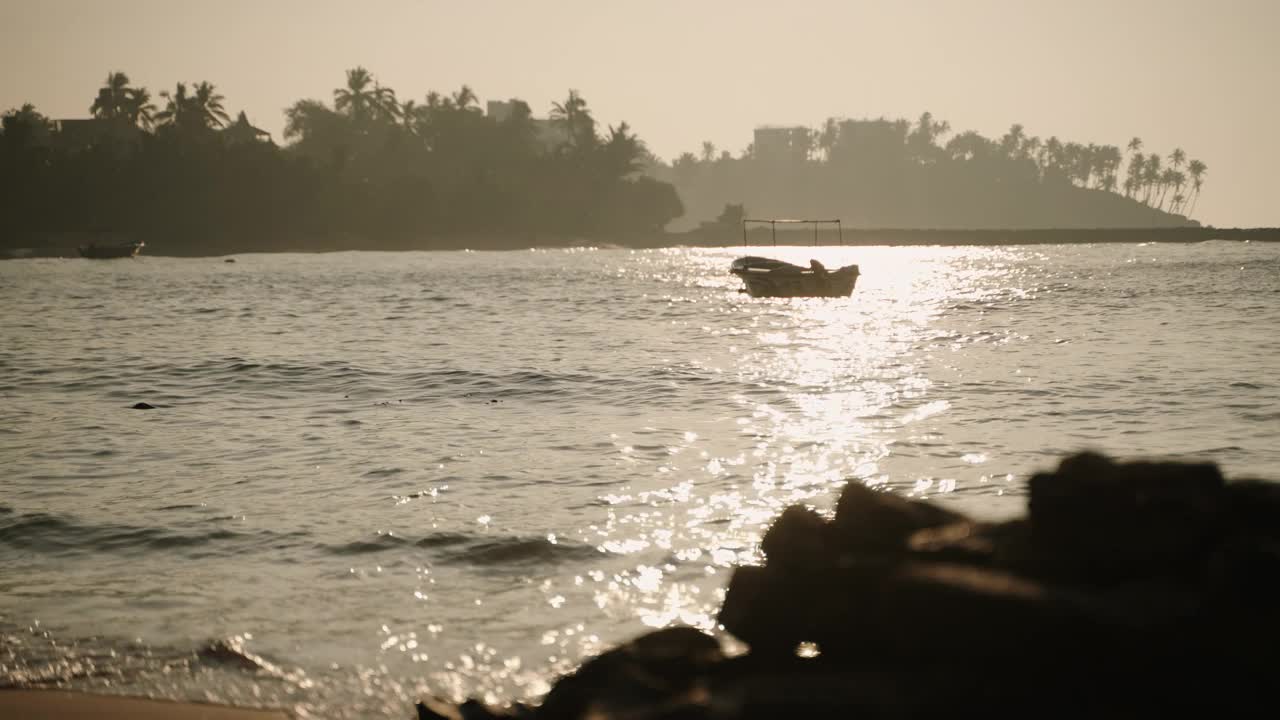 夕阳下，空船在海浪上摇摆。在落日的余晖中，棕榈树和酒店建筑的剪影以荒芜的海湾为背景。黄昏时平静的海水反射出的阳光。视频素材