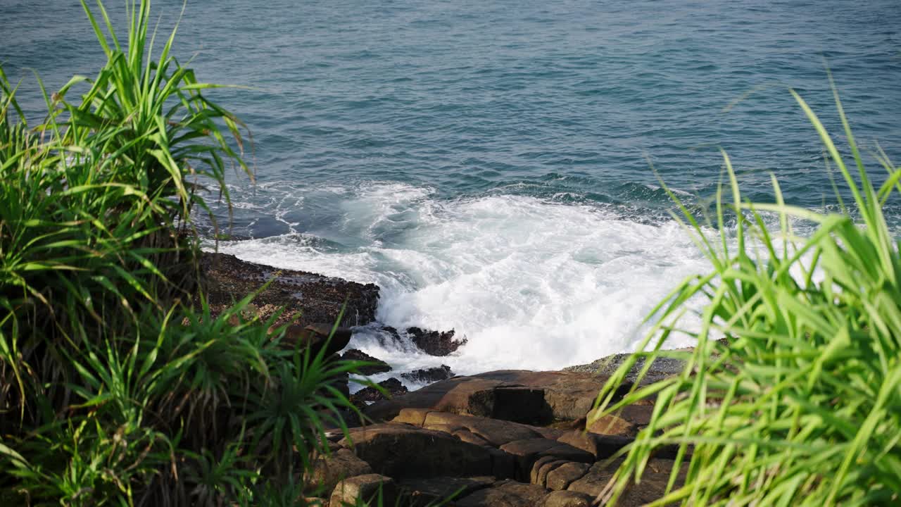 汹涌的海浪冲击着绿树成荫的岩石海岸线。海岸风光展现大自然的力量，海滨景观的宁静，海与陆的互动。视频素材