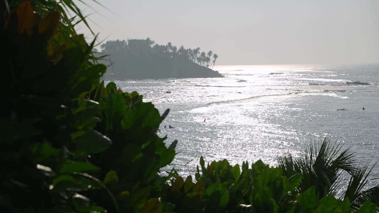 波光粼粼的海浪冲击着岩石海岸，前景郁郁葱葱。黄金时刻的宁静海景，水面反射的阳光，宁静的自然景象。热带景色描绘了海洋的壮丽视频素材