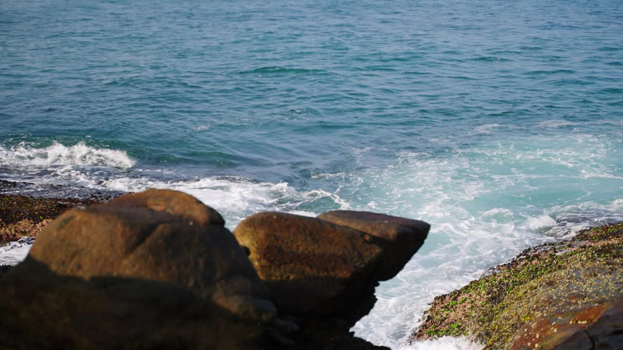 雄伟的海浪冲击着海边的岩石，海岸附近的浪花在阳光下闪闪发光。清澈湛蓝的海水显示出海洋的力量。热带景色描绘了海洋的壮丽。沿海景观视频素材