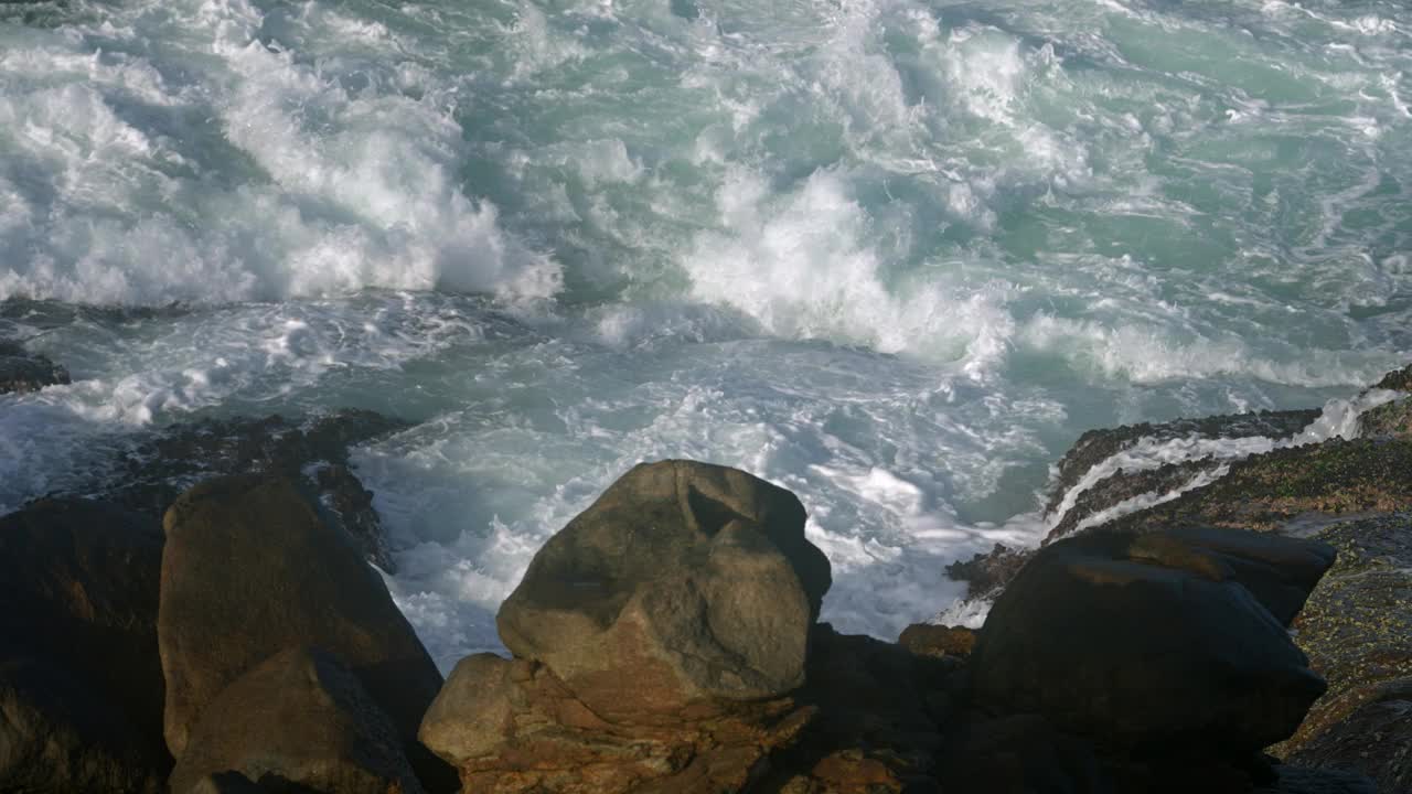 碧绿的海浪冲击着崎岖的海岸岩石，浪花飞溅。海景描绘了自然的力量，海岸侵蚀的作用。海景观，动态波浪运动，海的自然力量视频素材