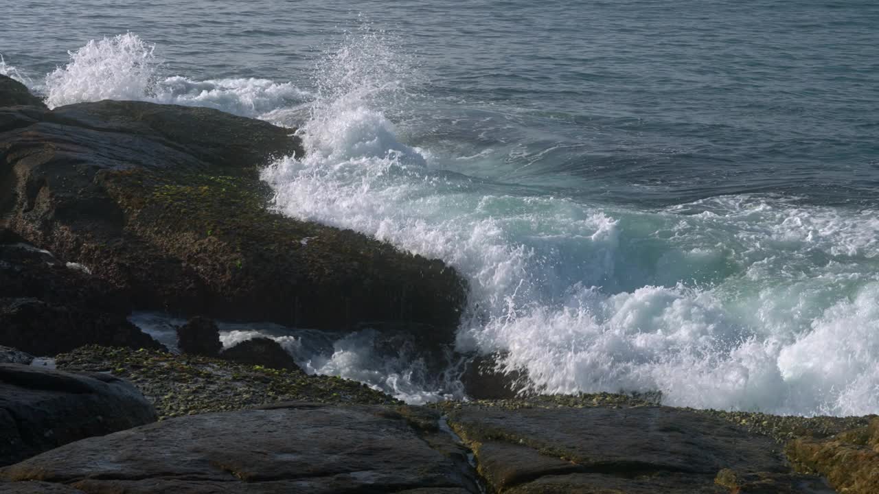 海浪冲击着岩石海岸，浪花飞溅。海水吞没了石头，退缩了。强大的海浪，海岸风光，自然力量的展示。海洋能源，海边岩石，潮汐冲击捕获。视频素材