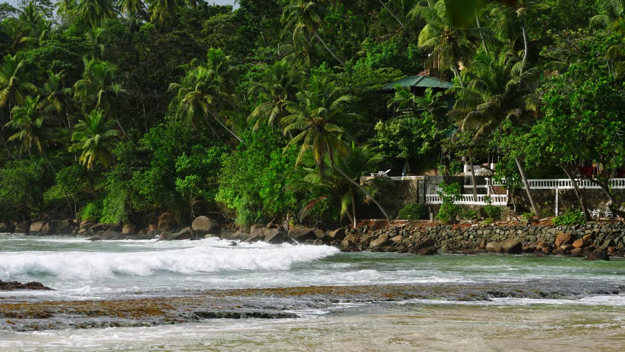 热带米丽莎海滩泻湖，斯里兰卡，海浪撞击岩石茂盛的棕榈树环绕小屋，幽静的天堂，理想的旅游，自然，沿海生态系统的保护展示。视频素材