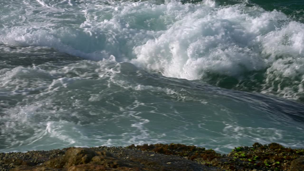 强大的海浪冲击着岩石海岸，浪花、泡沫在海岸风景中形成。动感的海洋力量，天然的水能量在海边展现。海水退去，露出苔藓覆盖的岩石。视频素材