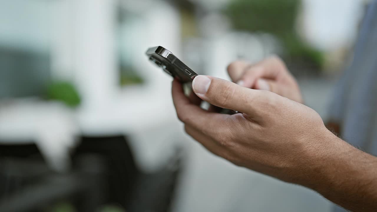 一个留着金色胡子的英俊年轻人，在城市的街道上拿着他的智能手机，发着技术娴熟的短信，在网上聊天。成年人与城市数字世界的联系。视频素材