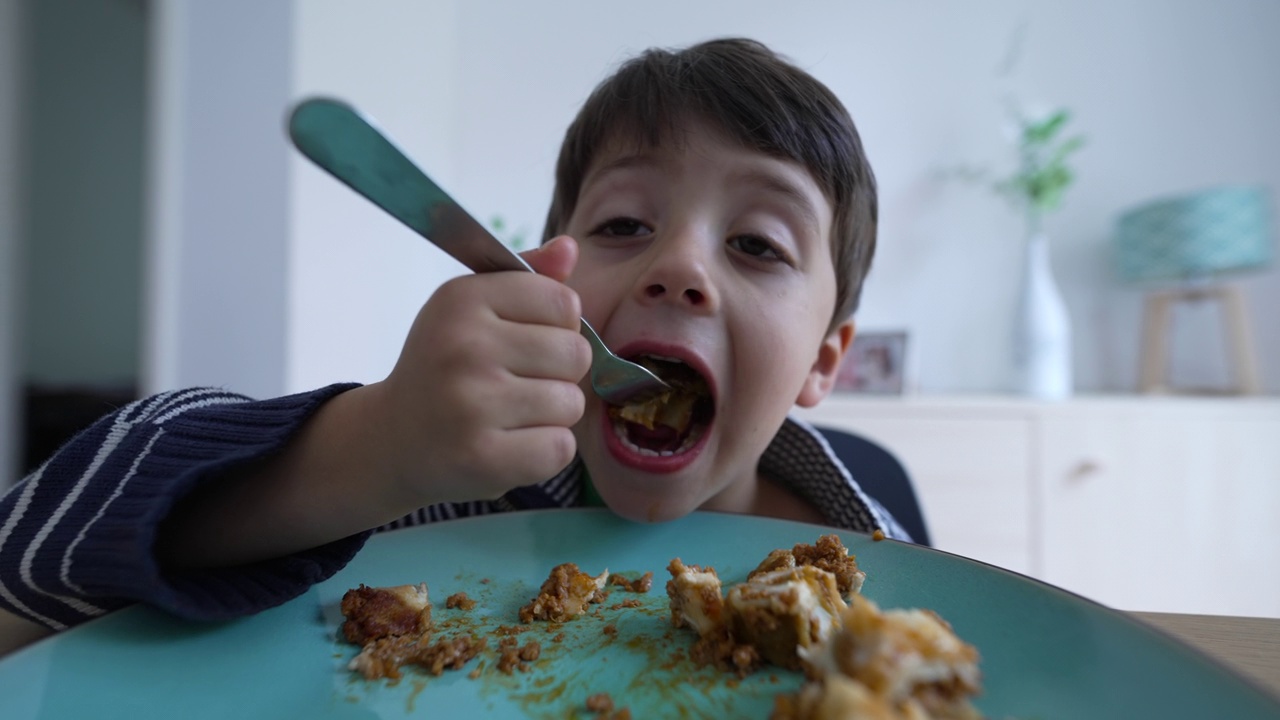 孩子的午餐-男孩在家里用叉子吃饭视频素材