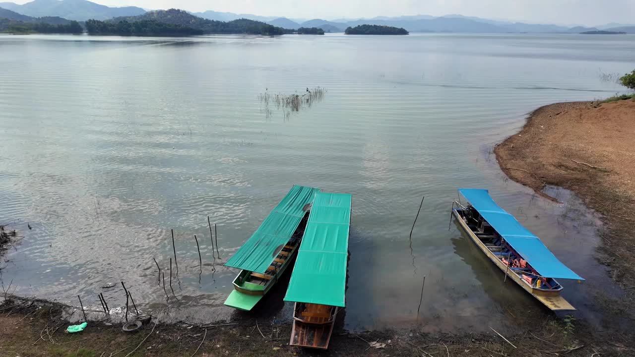 三艘船停靠在湖岸，在阳光明媚的一天，蓝天白云的山脉背景在泰国康克拉山国家公园。视频下载