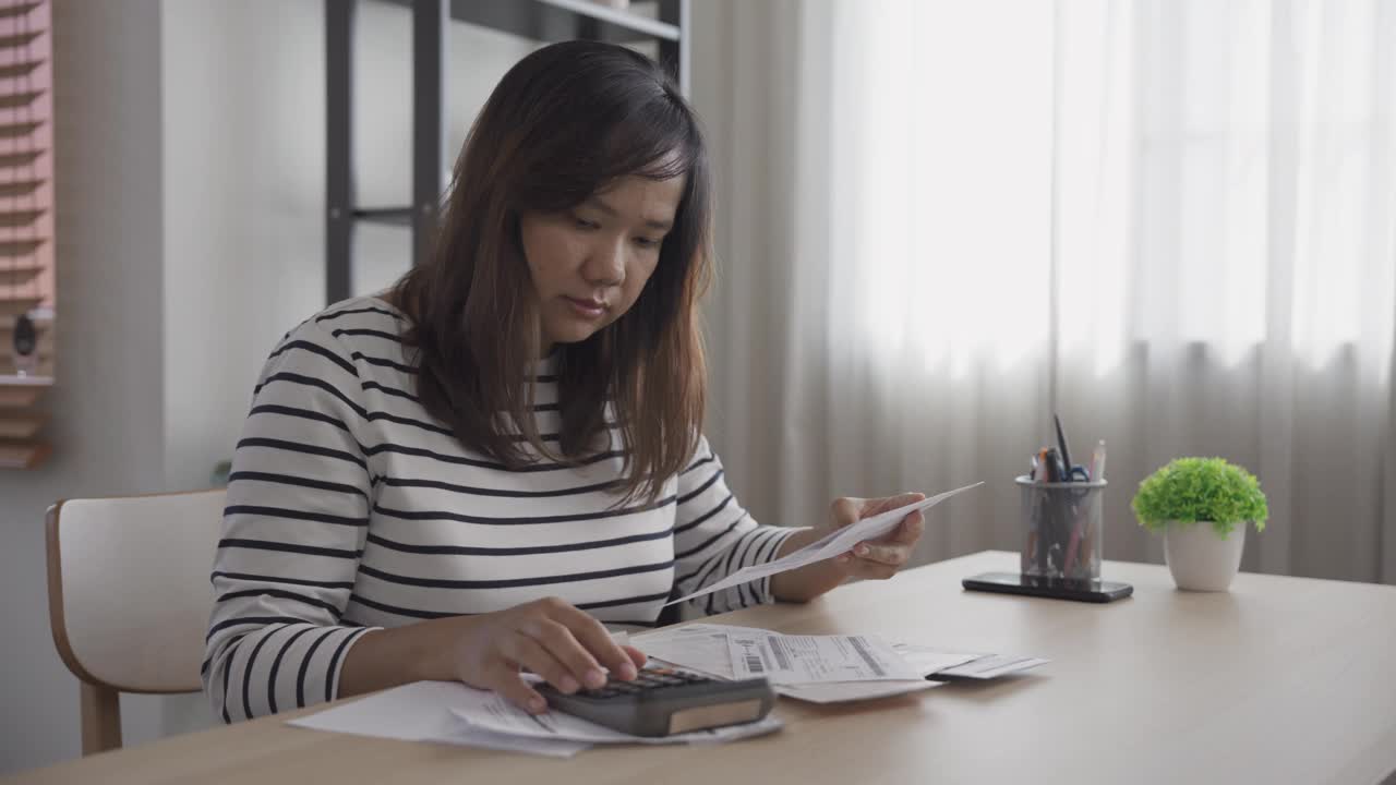 一名亚洲妇女用计算器分析和计算住房贷款、水电费和金融账单视频素材