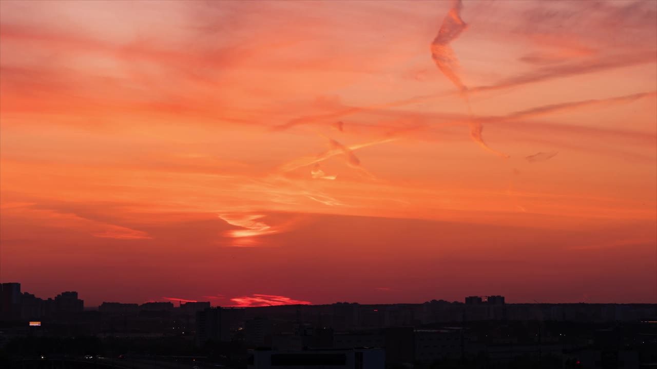 夜晚城市的时间流逝。市中心建筑物的剪影和被照亮的高速公路出现在明亮的橙色和红色夕阳天空的背景上视频下载