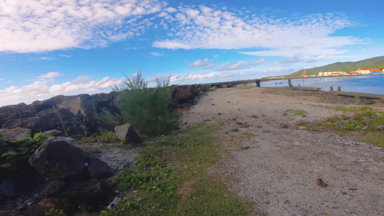 沿着岩石海岸线，从泻湖和环礁海洋咸水中保护，在良好的风化日蓝天阳光下，沿着阿瓦蒂乌港周围的沙湾地区向前行走视频素材