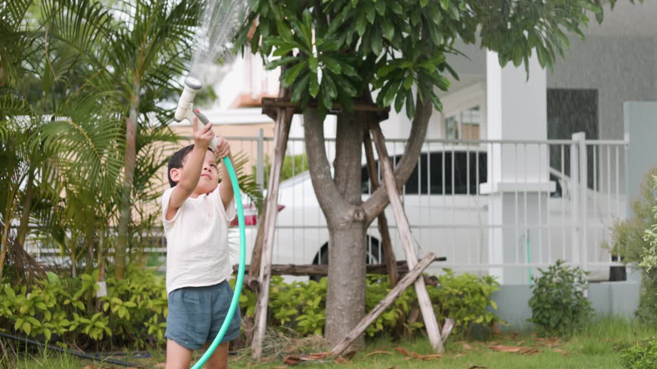 快乐的小男孩在花园里给植物和草坪洒水视频素材