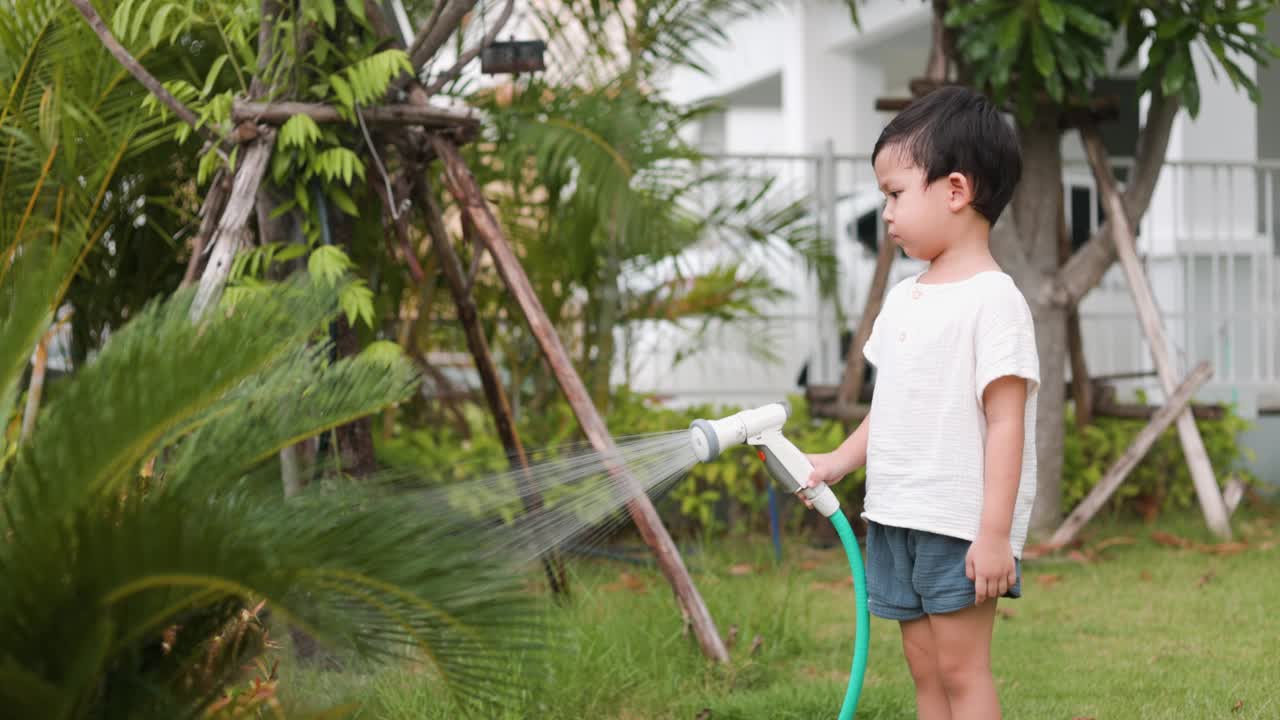 快乐的小男孩在花园里给植物和草坪洒水视频素材