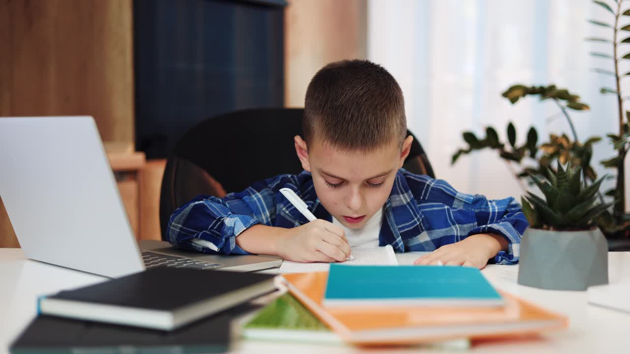 忙碌的男学生在家里的网络课堂上做笔记。漂亮的白人男孩穿着休闲装，用现代笔记本电脑与老师远程交流。视频素材