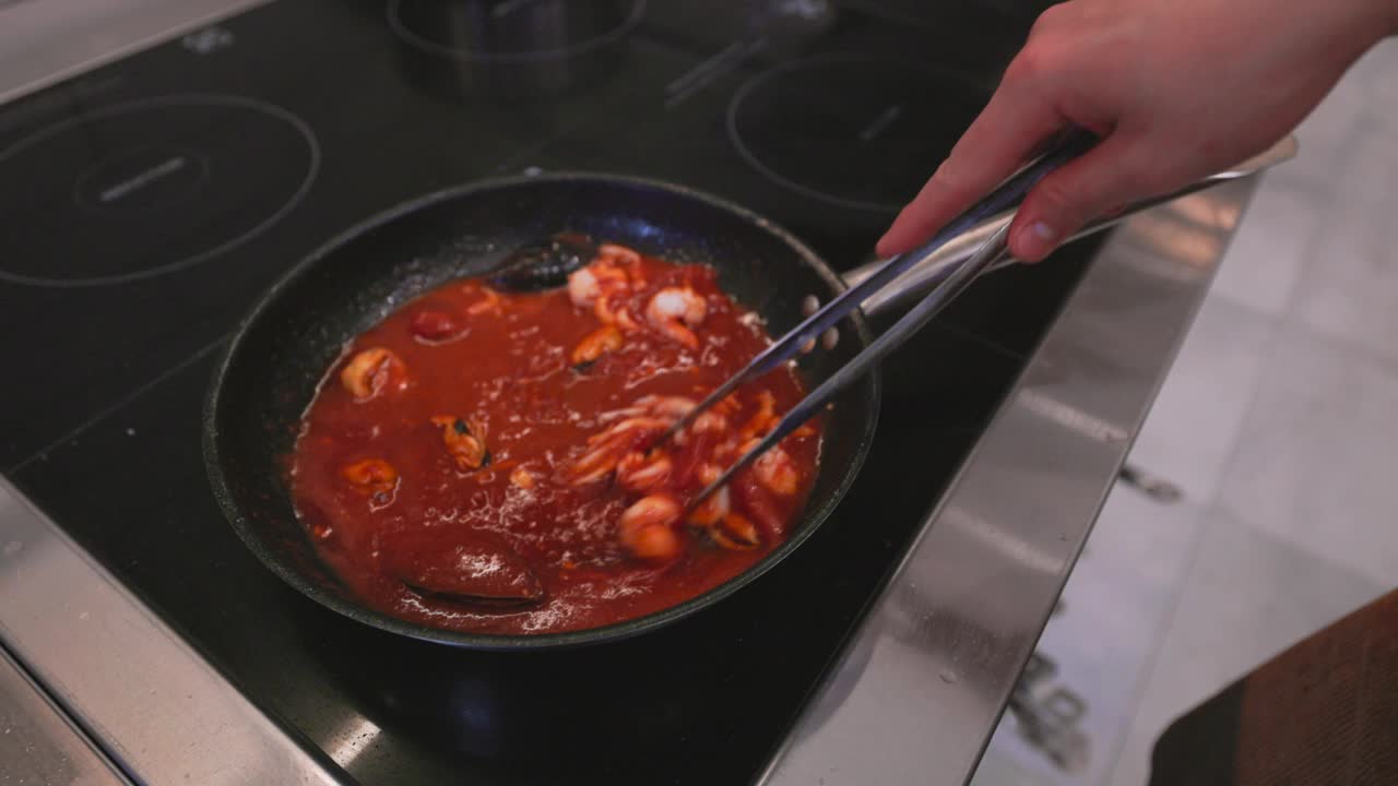 意大利面食:用海鲜烹饪的过程。煮熟的意大利面与酱汁和配料混合在热锅里。意大利菜，传统食谱。慢动作视频视频素材