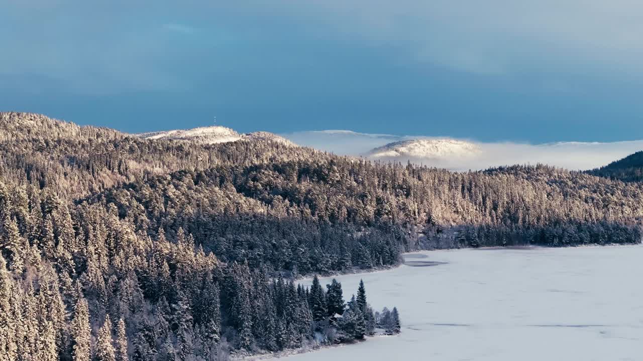 挪威因德福森的冰湖、白雪覆盖的松树林和冬季的山脉。-航拍视频素材