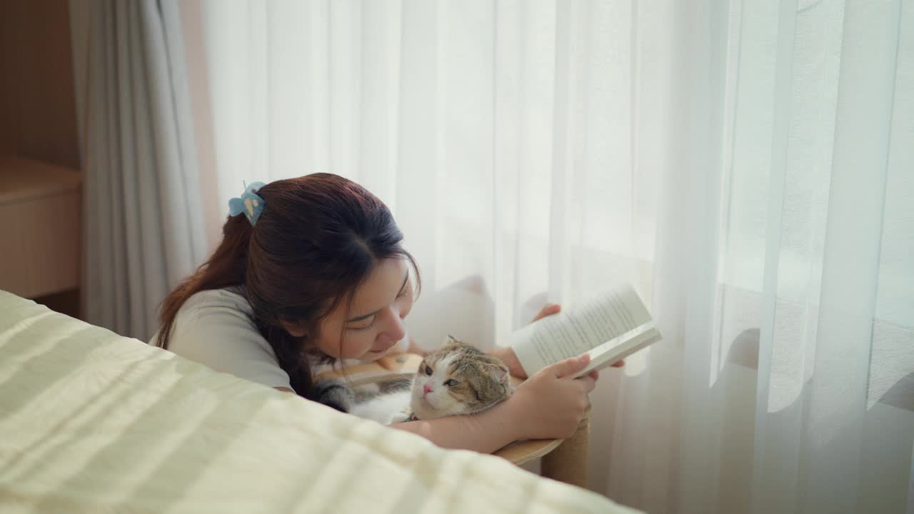 年轻女子在一个房间里和猫一起看书视频素材