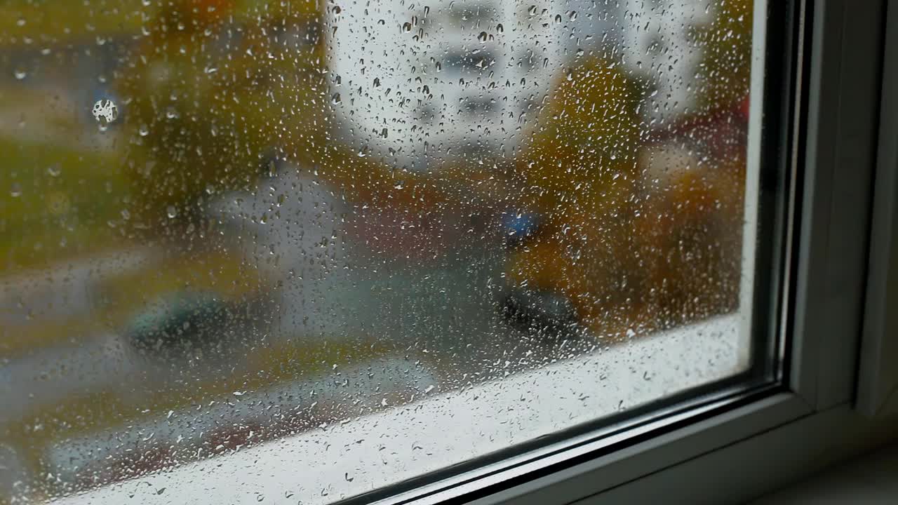 从屋内望向街道，雨滴落在窗台和双层玻璃上。秋天天气寒冷。文本的复制空间，凹陷视频素材