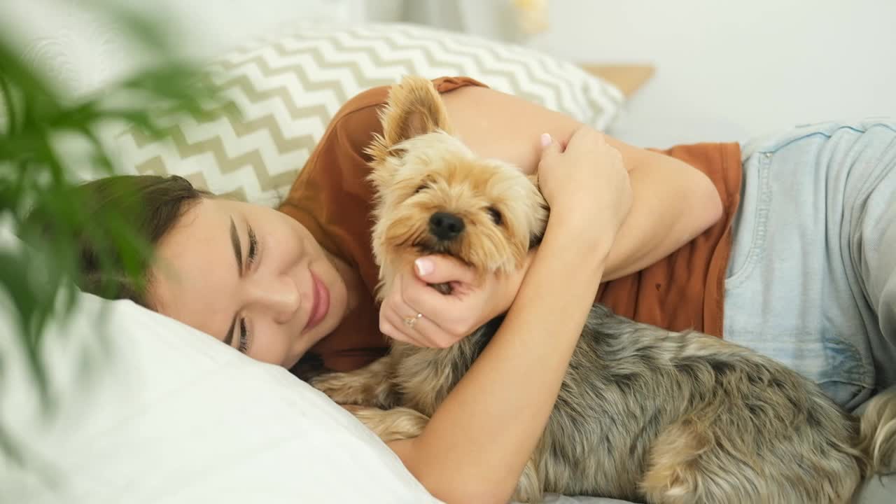 一个年轻的女人正躺在床上和她的狗玩。视频下载