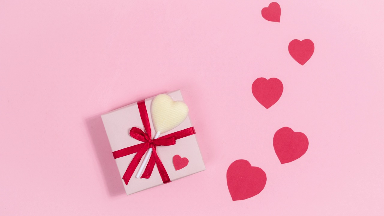 粉色礼盒旁系着红丝带和白色巧克力心形糖果，爱心飞逝，象征着爱。情人节贺卡。视频下载