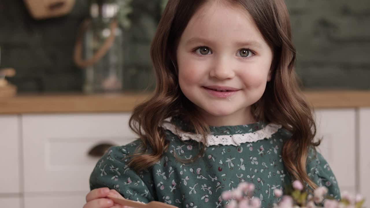 4-5岁的开朗小女孩的肖像，穿着节日时尚的复古绿色花裙，准备在时尚的家庭厨房里庆祝她的生日和吃蛋糕。儿童节。视频素材