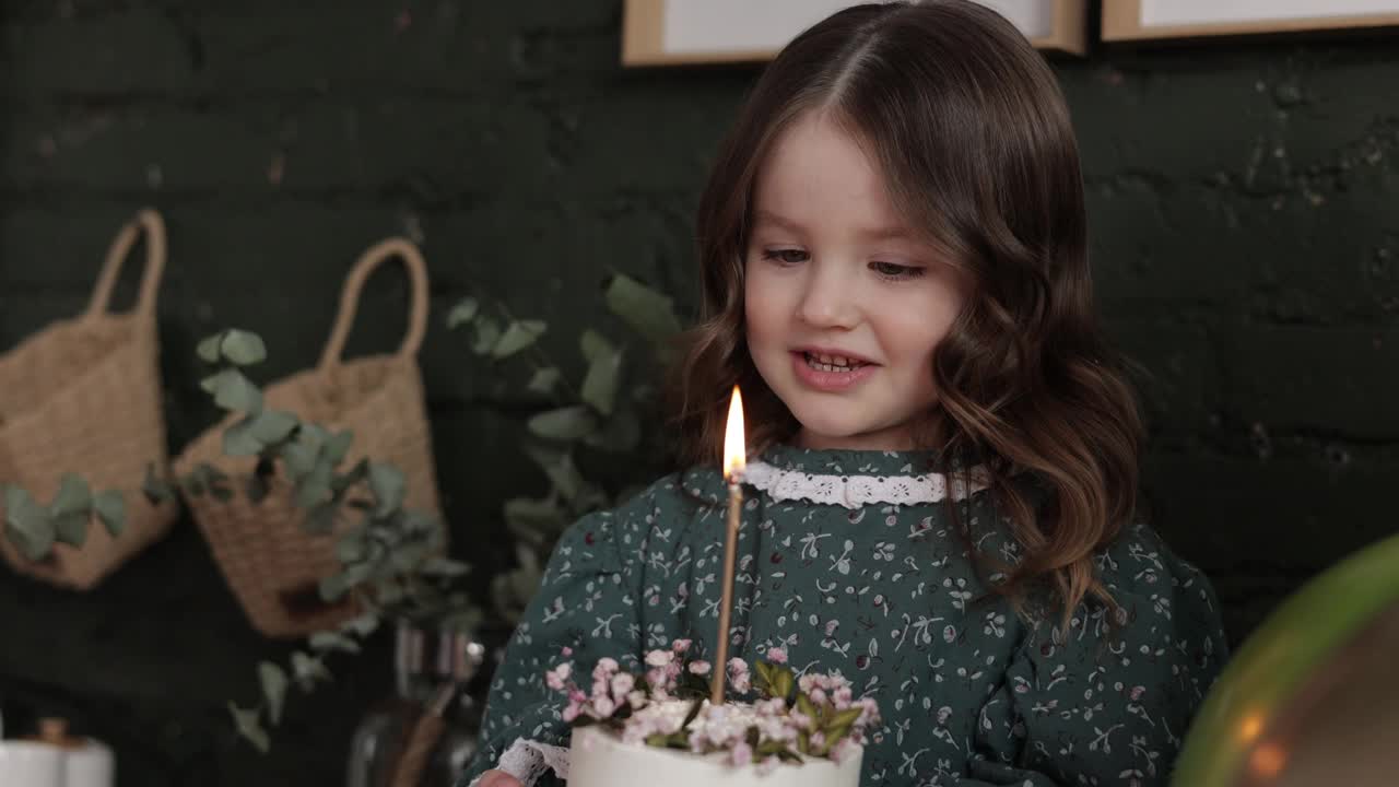 可爱的小女孩4-5岁拿着白色的生日蛋糕装饰着鲜花和试图吹燃烧的蜡烛。孩子穿着节日时尚的复古连衣裙准备在家里参加她的生日派对视频素材