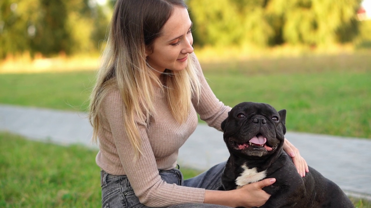 快乐的女人在后院散步时抚摸和亲吻黑色的法国斗牛犬。人类和狗的友谊概念视频素材