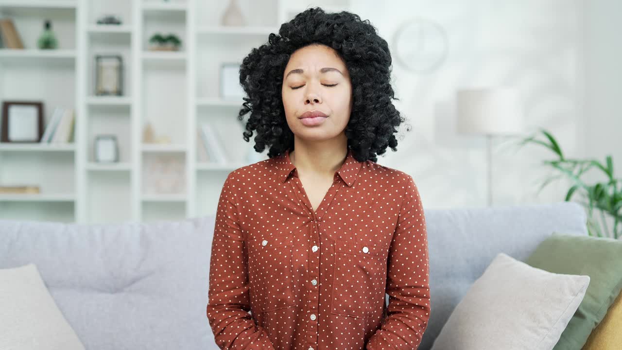 可怜的年轻非裔美国女性，正因牙痛而坐在家里的沙发上。视频素材