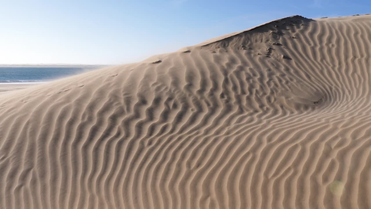 大风把沙子吹过沙丘的山脊，吹向大海。奈拉湖，撒哈拉沙漠与大西洋的交汇处，摩洛哥肯尼菲斯国家公园。视频素材