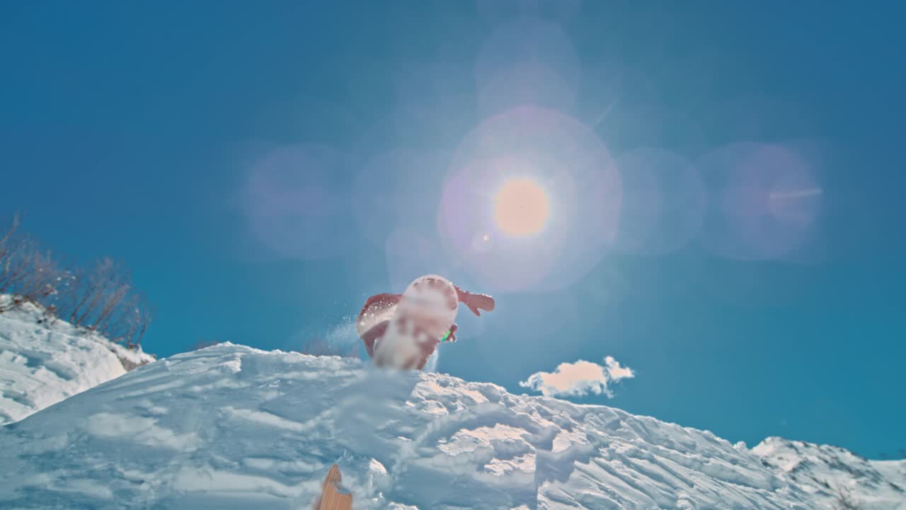 在阳光明媚的日子里，滑雪板运动员的SLO MO对着天空。男子正在雪山上玩单板滑雪。他正在享受假期。视频下载