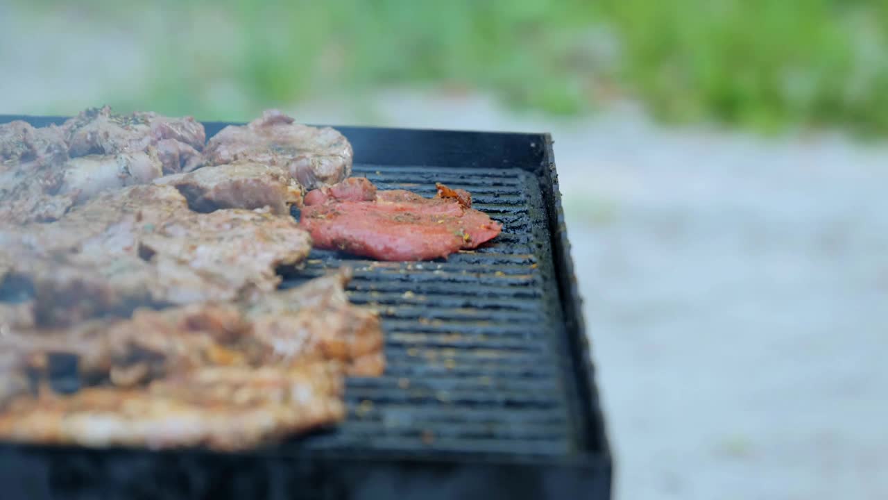 在户外烧烤。在燃烧的火上烤着一块生肉牛排，一个男人用夹子在烧烤架上翻转烤好的牛排。美味烤肉的特写镜头。视频素材