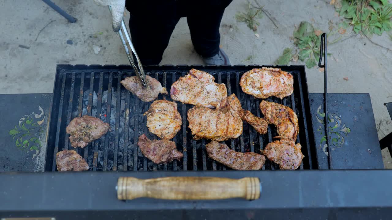 烧烤烟和火焰，烤肉在火上。在户外烧烤。在燃烧的火上煎生肉牛排，一个人用钳子。在烤架上烤牛排的特写。夏日野餐概念视频素材