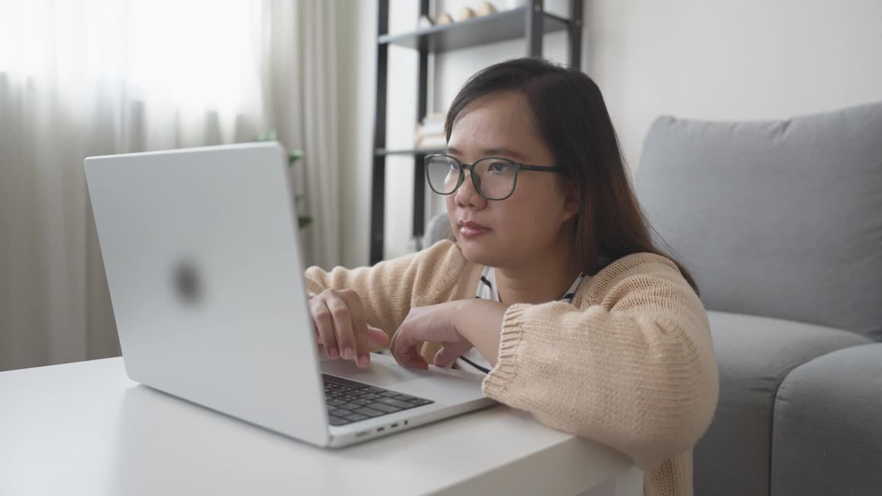 亚洲女人坐在地板上用笔记本电脑在客厅工作视频素材