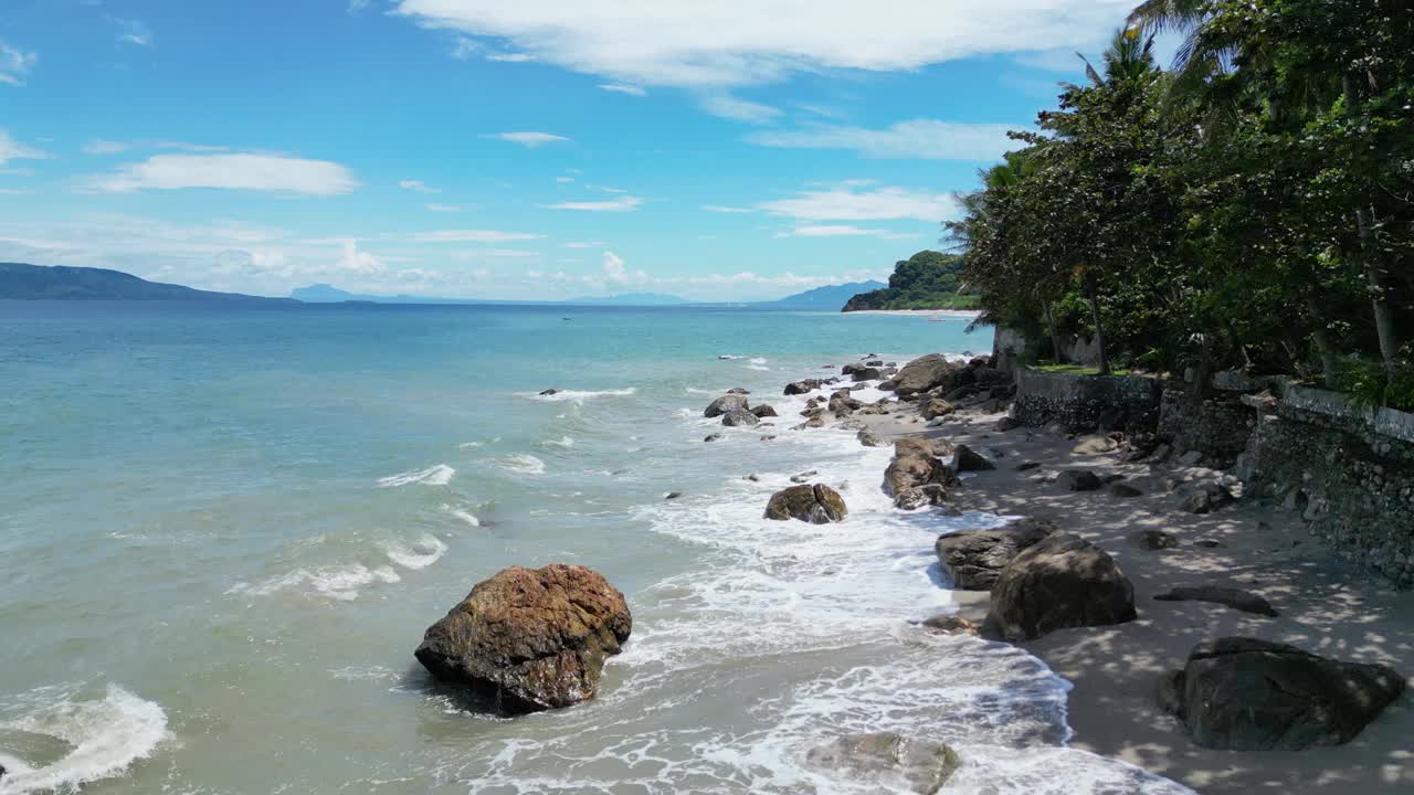 海滩上有被海水冲刷的岩石和海岸上的热带树木视频素材