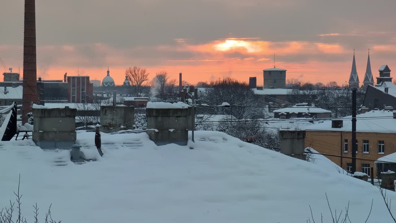 在城市工业区的屋顶上，雪花缓缓落下，太阳在灰色的冬日天空中发出橙色的光芒视频素材