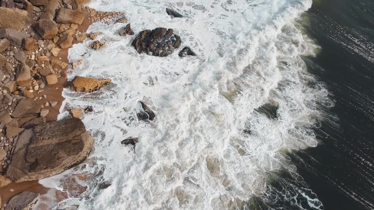 鸟瞰图，海浪在葡萄牙纳扎雷的岩石海岸线上破碎。在这里，海洋的力量与岩石海岸的多样性相遇。原始自然概念。4 k。视频素材