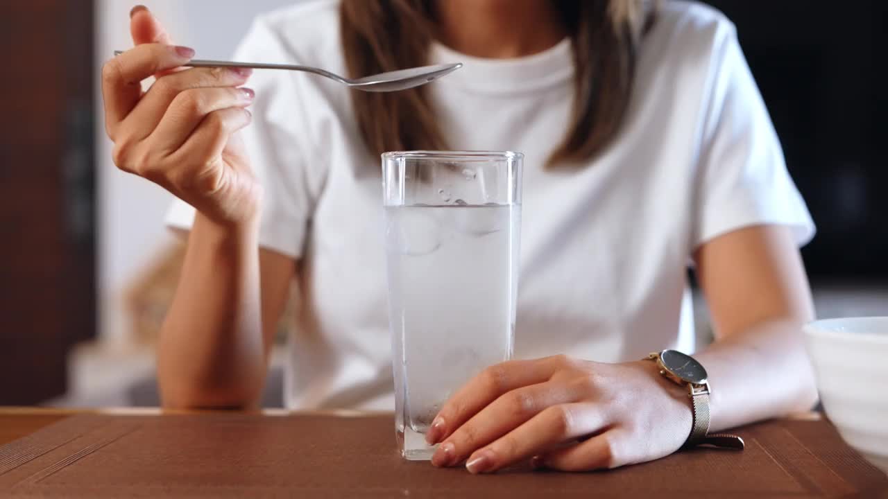 一名亚洲妇女坐在餐厅里，用勺子把一杯水中的冰舀掉视频素材