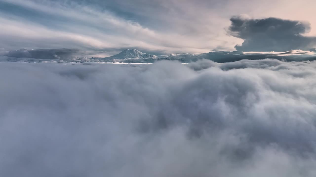 日落时在云层上低空飞行的鸟瞰图。夕阳下沉睡的厄尔布鲁士火山。云冲浪视频素材