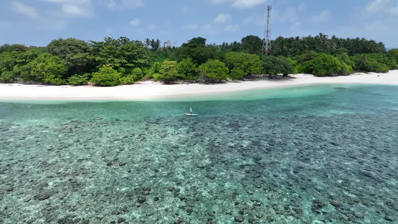 一个美丽的女孩优雅地在绿松石般的马尔代夫水域上划桨，从上面拍摄的令人惊叹的鸟瞰图视频素材