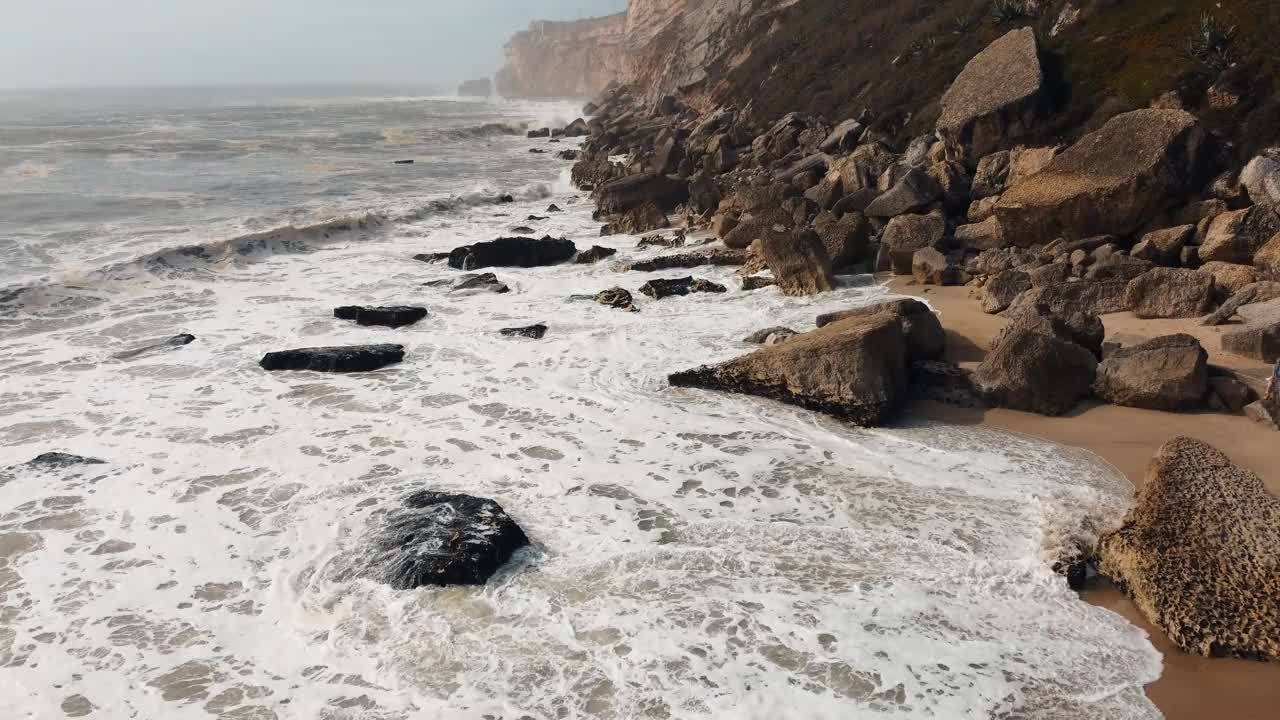 航拍镜头捕捉到海浪冲击葡萄牙纳扎雷崎岖海岸的不屈不挠的力量。海洋的不可驯服的力量展现出来。4 k。视频素材