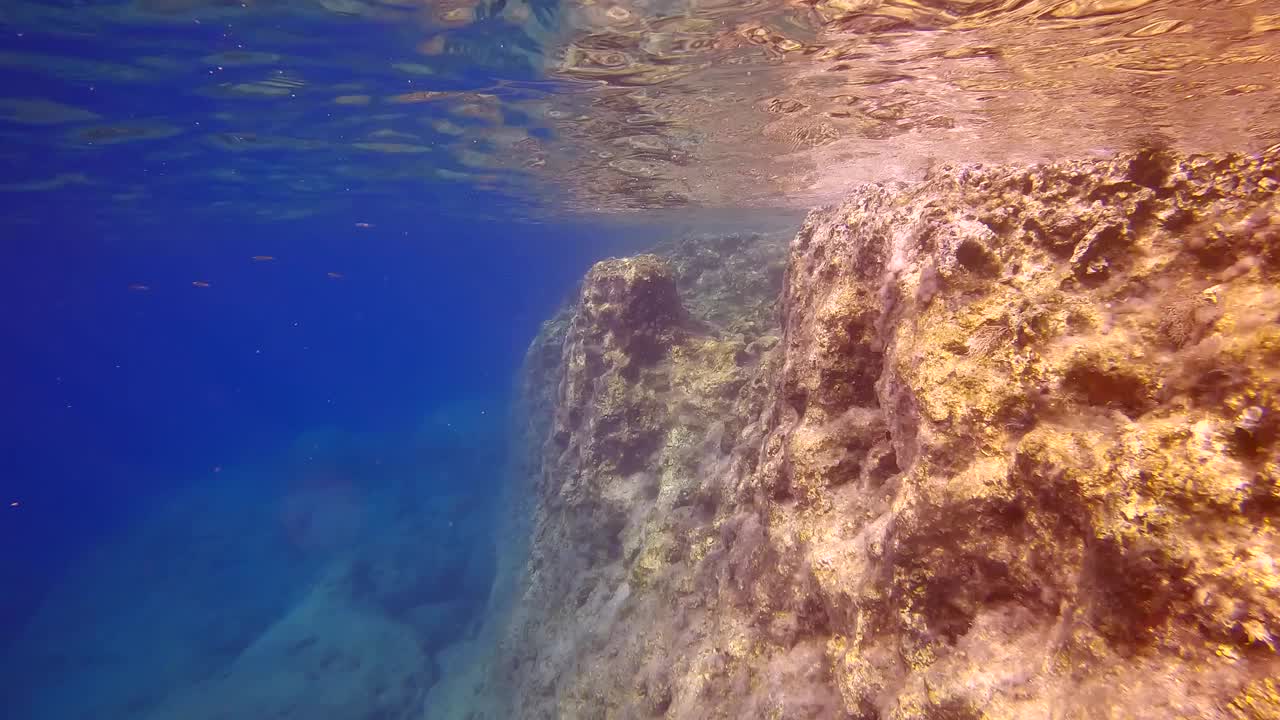 相机沿着陡峭的悬崖向前移动，反射在水面上，在蓝色的水背景视频素材