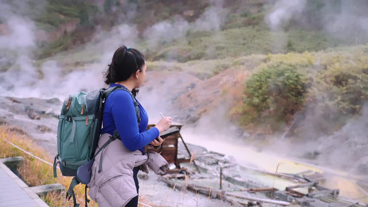 一位亚洲女性环保人士在日本东北秋田附近的森林里观察温泉，并将数据记录在她的数码平板电脑上，用于她的环境研究。视频素材