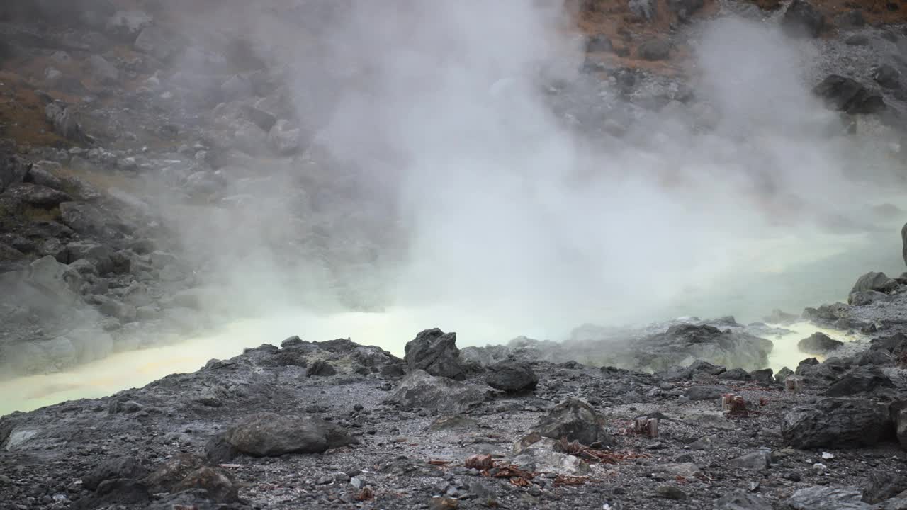 宁静的场景，沉重的白色蒸汽和硫磺从地热温泉上升，设置在日本东北秋田多摩川温泉的森林山丘的背景下，邀请自己沉浸在这个自然天堂的舒缓气氛中。视频素材