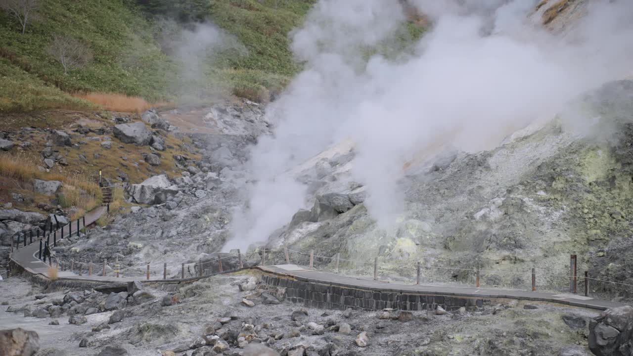 独特的地热能景观，厚重的蒸汽和大量的硫磺矿物在山上，中间的小径被建筑包围，坐落在郁郁葱葱的山麓上。视频素材