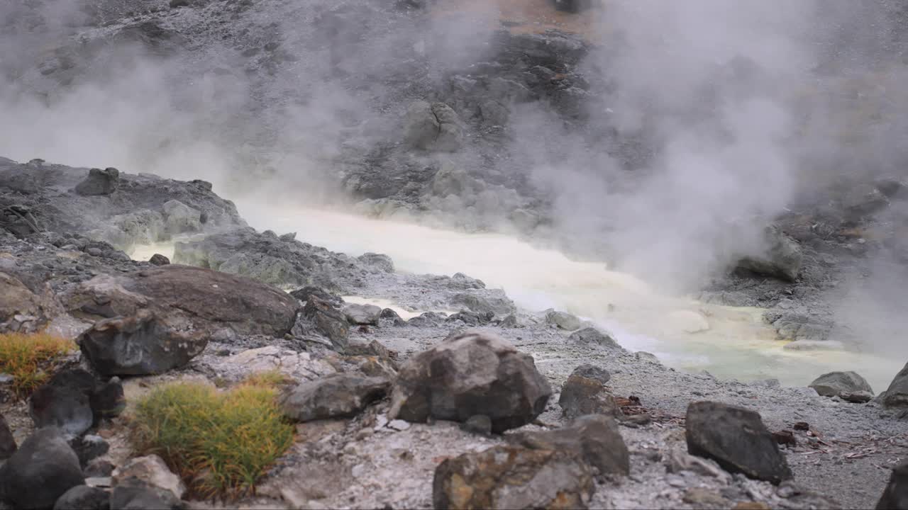 近距离拍摄的蒸汽从日本东北秋田多摩川温泉附近的地热温泉中升起，展示了人类活动与自然保护之间的和谐平衡。视频素材