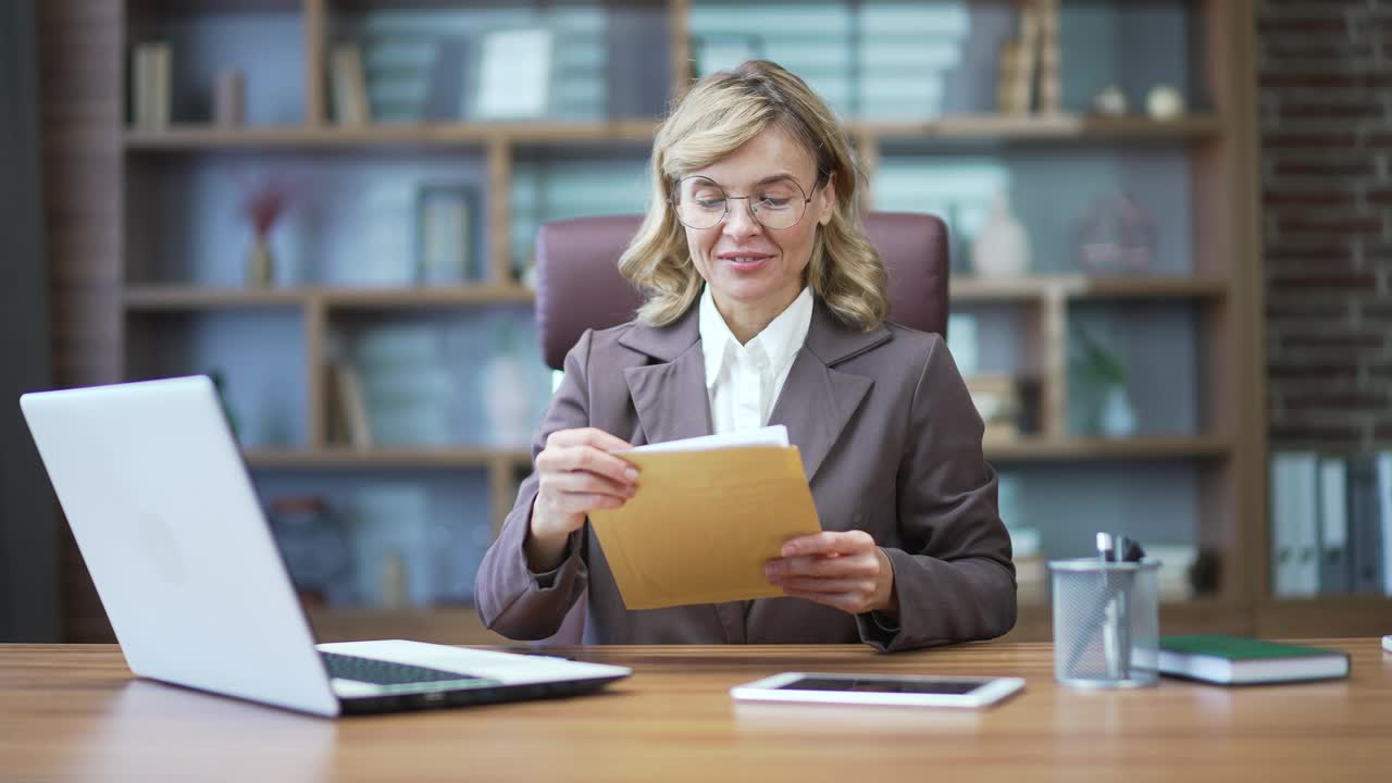 快乐成熟的女商人坐在办公室里读着带着好消息的信。女性企业家,视频素材